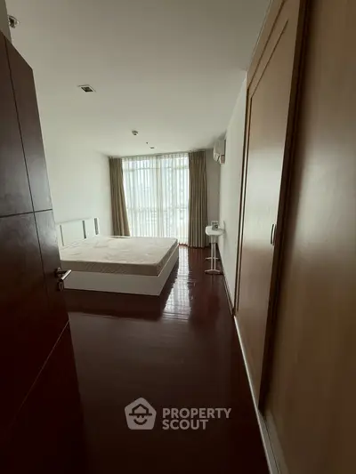 Spacious bedroom with large window and wooden flooring, offering ample natural light and cozy ambiance.