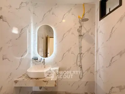 Elegant bathroom with marble tiles and modern fixtures, featuring a stylish oval mirror and rainfall showerhead.