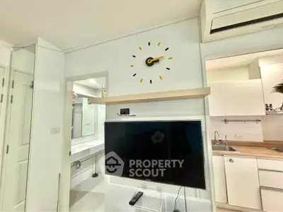 Modern living room with wall clock and TV, adjacent to a sleek kitchen