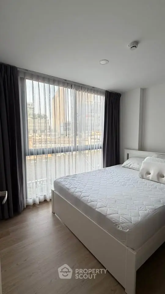Modern bedroom with large window and city view, featuring a comfortable bed and stylish decor.