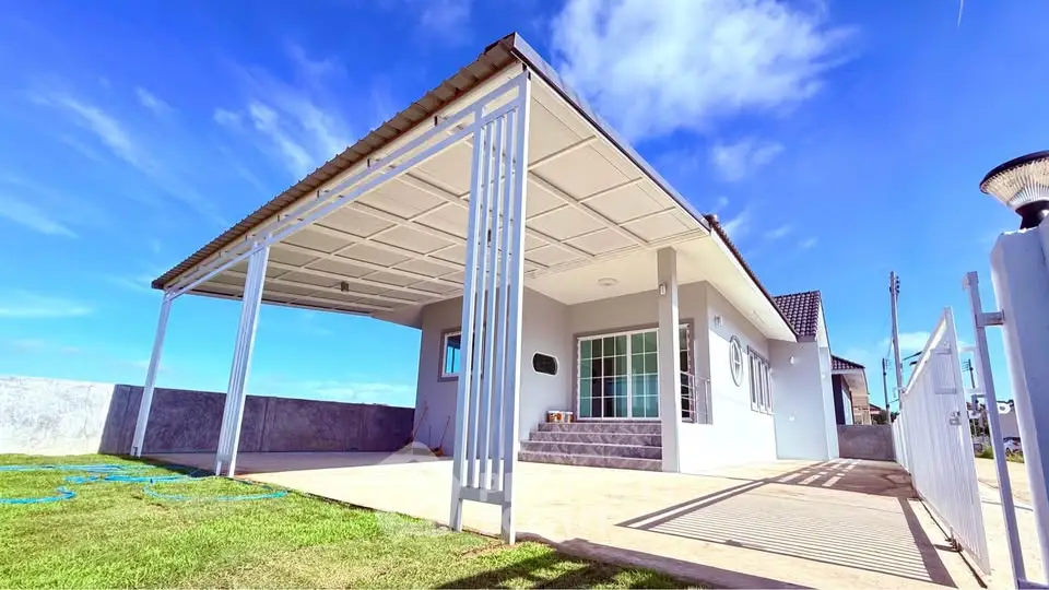 Modern single-story house with spacious carport and lush green lawn under a clear blue sky.