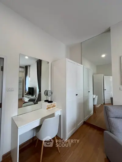 Modern bedroom with sleek white furniture and wooden flooring, featuring a stylish vanity and wardrobe.