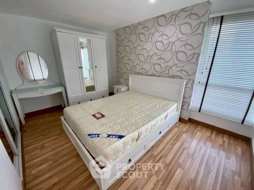 Cozy bedroom with stylish wallpaper and wooden flooring, featuring a white bed and wardrobe.