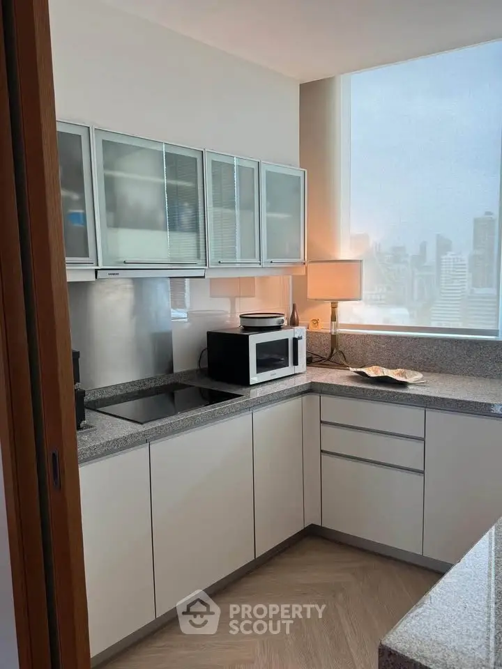 Modern kitchen with sleek cabinets and city view, featuring a microwave and elegant lighting.