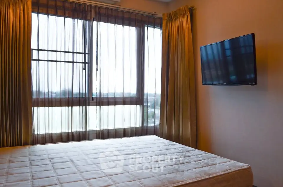 Cozy bedroom with large window and wall-mounted TV, offering a serene view.