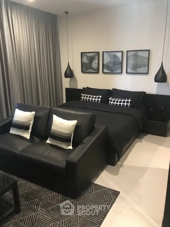 Modern bedroom with stylish black decor, featuring a cozy bed, sleek sofa, and elegant pendant lights.