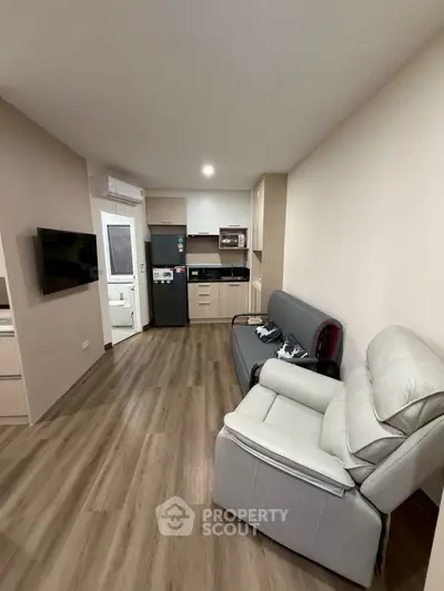 Modern living room with open kitchen, featuring sleek appliances and cozy seating area.