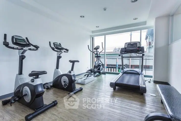 Modern gym with exercise equipment and large windows in a residential building.