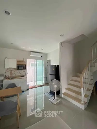 Modern open-plan living area with kitchen and staircase, featuring sleek design and natural light.