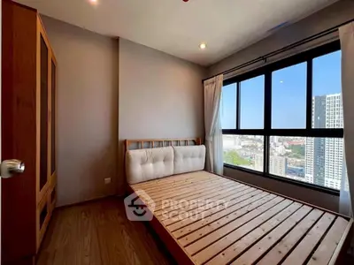 Cozy bedroom with large window offering stunning city views, featuring wooden flooring and minimalist decor.