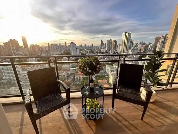 Stunning city view from a high-rise balcony with cozy seating and lush plants.