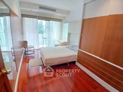 Spacious bedroom with wooden flooring and large windows in modern apartment.