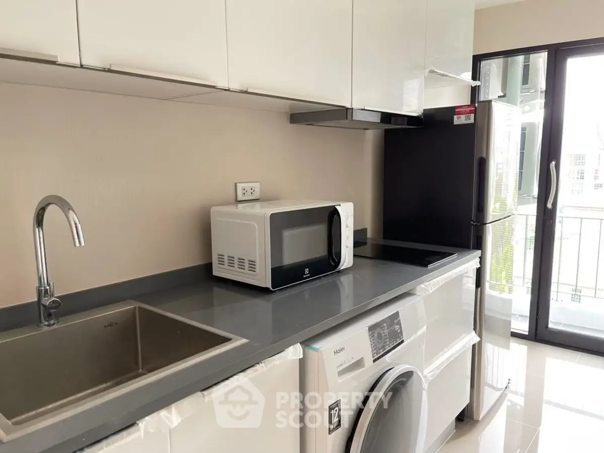 Modern kitchen with sleek appliances and balcony view, featuring microwave and washing machine.