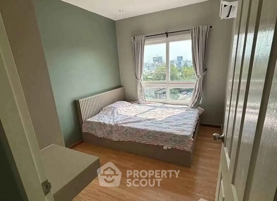 Cozy bedroom with large window offering city views, featuring wooden flooring and modern decor.