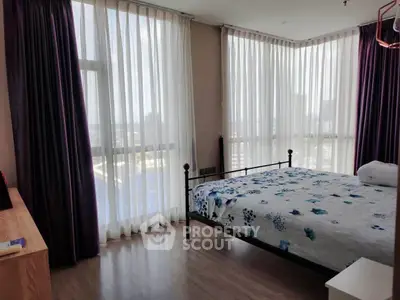 Spacious bedroom with large windows and elegant curtains, offering a bright and airy atmosphere.