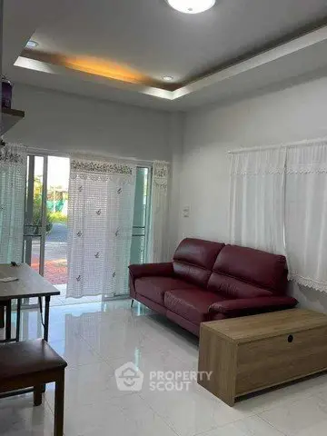 Cozy living room with red leather sofa and natural light from large windows.