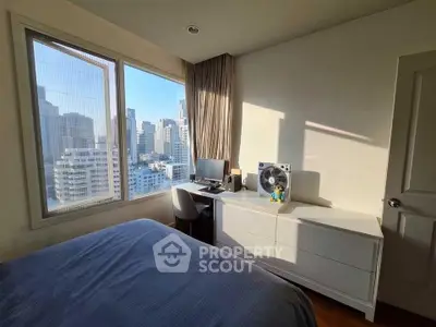 Modern bedroom with city view, featuring a cozy workspace and ample natural light.