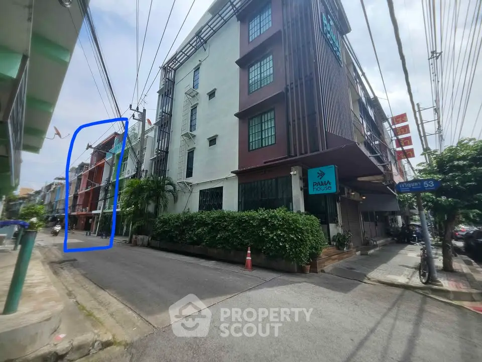 Street view of modern apartment building with lush greenery and clear sky.