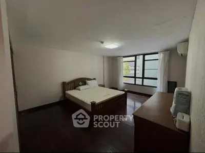 Spacious bedroom with wooden flooring and large window for natural light.