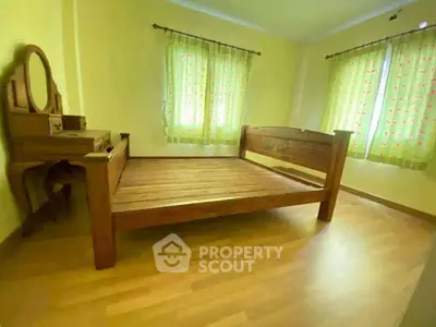 Cozy bedroom with wooden bed and vanity, bright natural light through patterned curtains.