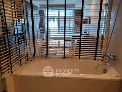 Modern bathroom with bathtub and window blinds offering a glimpse into a stylish living area.