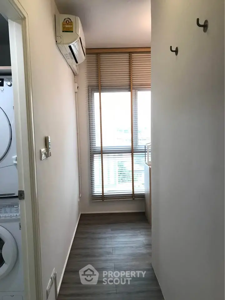 Compact laundry area with stacked washer and dryer, air conditioning, and window view.
