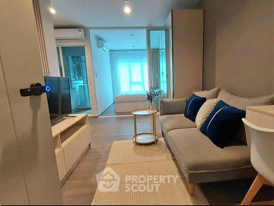 Modern living room with cozy sofa and view into bedroom, featuring sleek design and natural light.