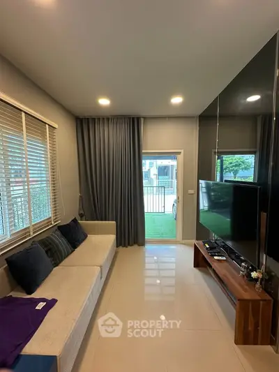 Modern living room with sleek furniture and large TV, leading to a garden view.