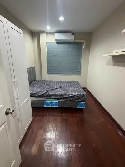 Cozy bedroom with wooden flooring and modern air conditioning unit, perfect for restful nights.