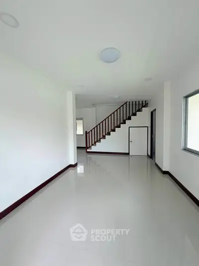 Spacious minimalist living room with sleek staircase and large window for natural light.