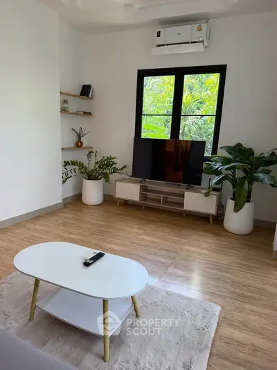 Modern living room with stylish decor, featuring a sleek TV setup, air conditioning, and lush greenery.