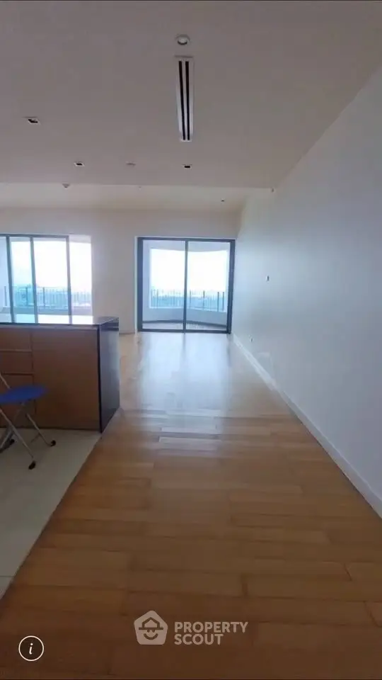 Spacious living room with wooden flooring and large windows leading to a balcony with a view.