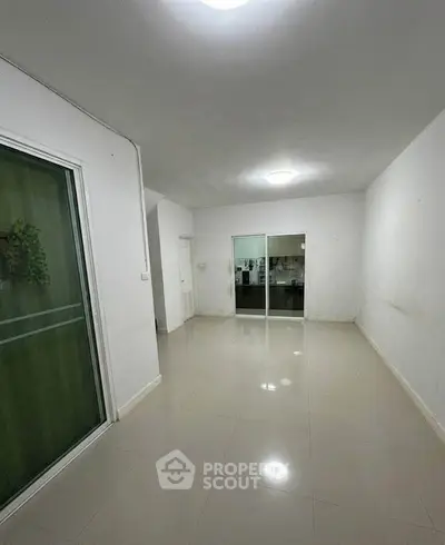 Spacious empty room with tiled flooring and sliding glass doors leading to another area.