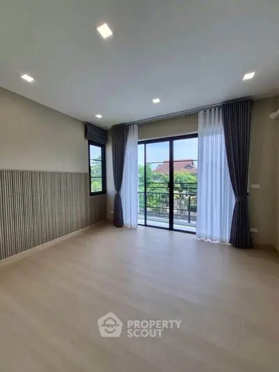 Spacious living room with large windows and balcony access, featuring elegant curtains and modern lighting.