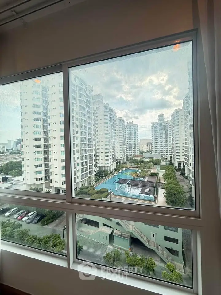 Stunning view of modern high-rise buildings with a pool from a window, showcasing urban living at its finest.