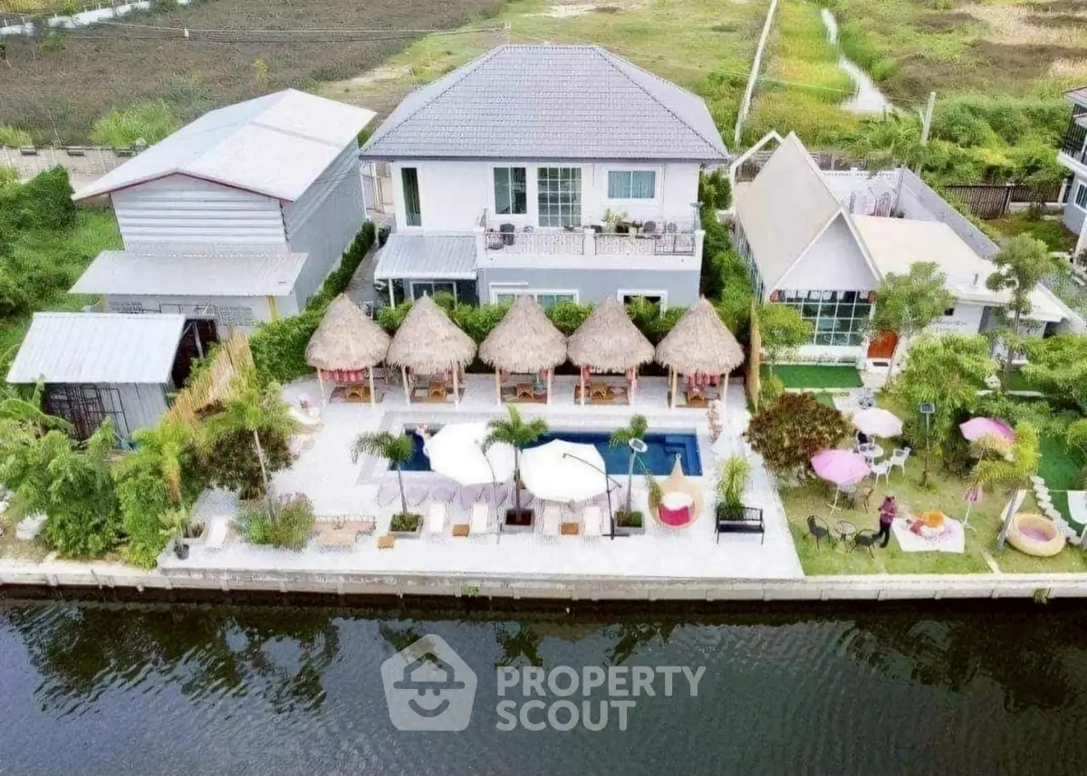 Stunning waterfront property with pool and thatched-roof cabanas, perfect for luxurious outdoor living.