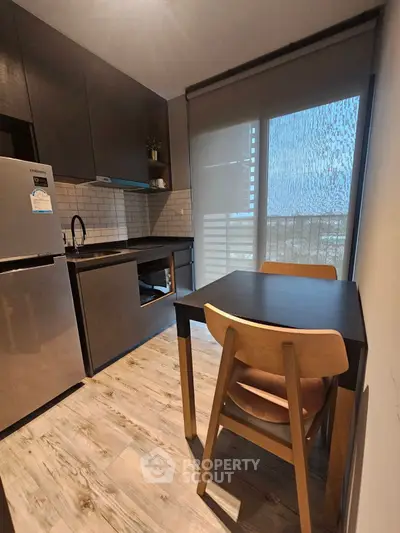 Modern kitchen with sleek design, featuring dark cabinets, stainless steel fridge, and cozy dining area.