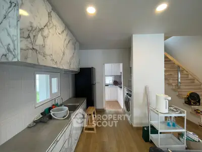 Modern kitchen with marble cabinets and wooden flooring, featuring a washing machine and open layout.