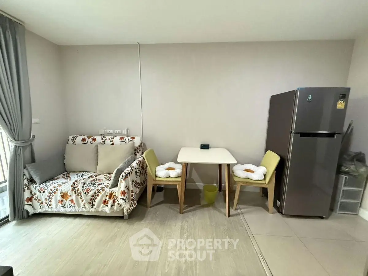 Cozy living room with floral sofa, dining table, and modern fridge in a bright apartment.