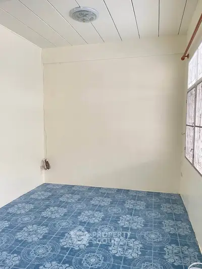 Spacious empty room with blue patterned tile flooring and large window, ideal for customization.