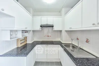 Modern kitchen with sleek white cabinets and black countertops, featuring a built-in stove and stainless steel sink.