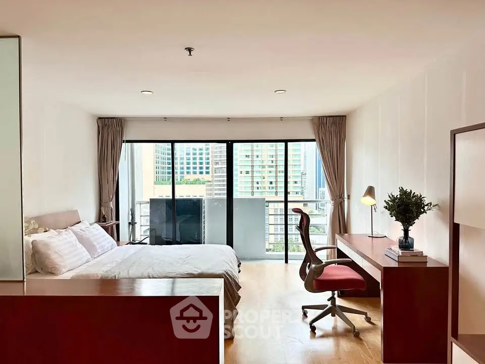 Spacious bedroom with balcony and city view, featuring modern furniture and natural light.