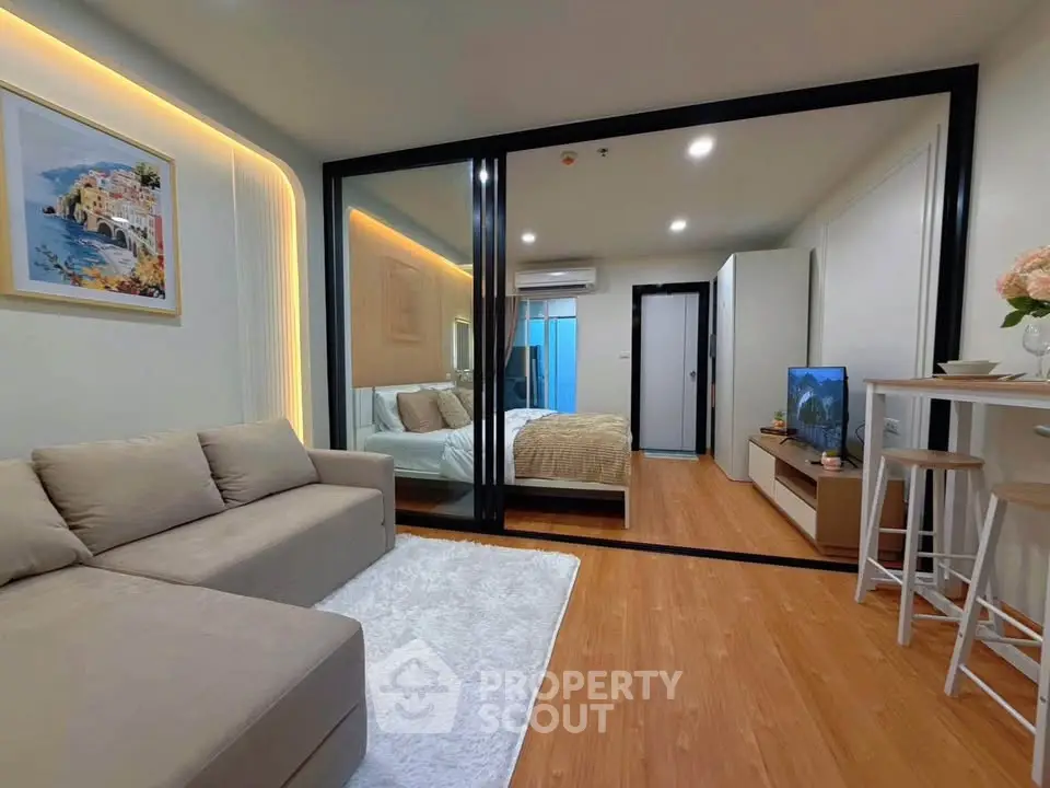 Modern living room with cozy sofa and stylish bedroom separated by glass partition.