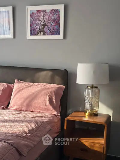 Cozy bedroom with pink bedding, elegant lamp, and framed art on gray wall.