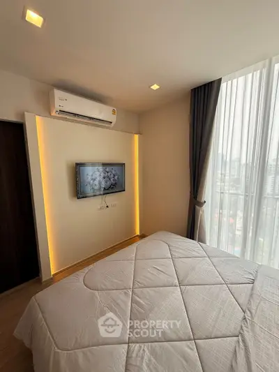 Modern bedroom with stylish decor and city view, featuring a wall-mounted TV and air conditioning.