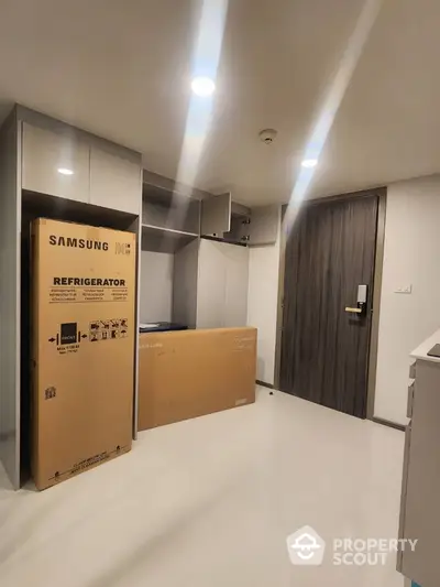 Modern apartment interior with new Samsung refrigerator in box, sleek cabinets, and polished flooring.