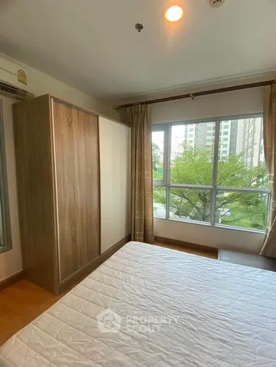 Cozy bedroom with large window and wardrobe offering a serene garden view.