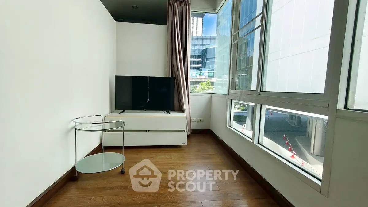 Modern living room with large windows and sleek TV stand in urban apartment.
