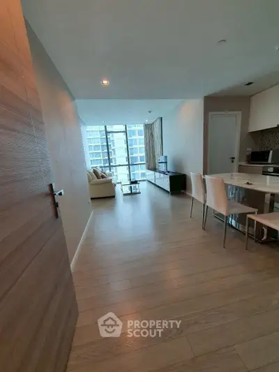 Modern open-plan living room with wooden flooring and large windows in a high-rise apartment.