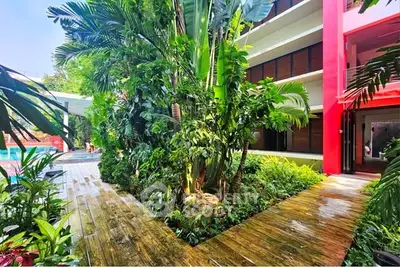 Lush tropical garden pathway in modern residential complex with vibrant red accents and pool view.